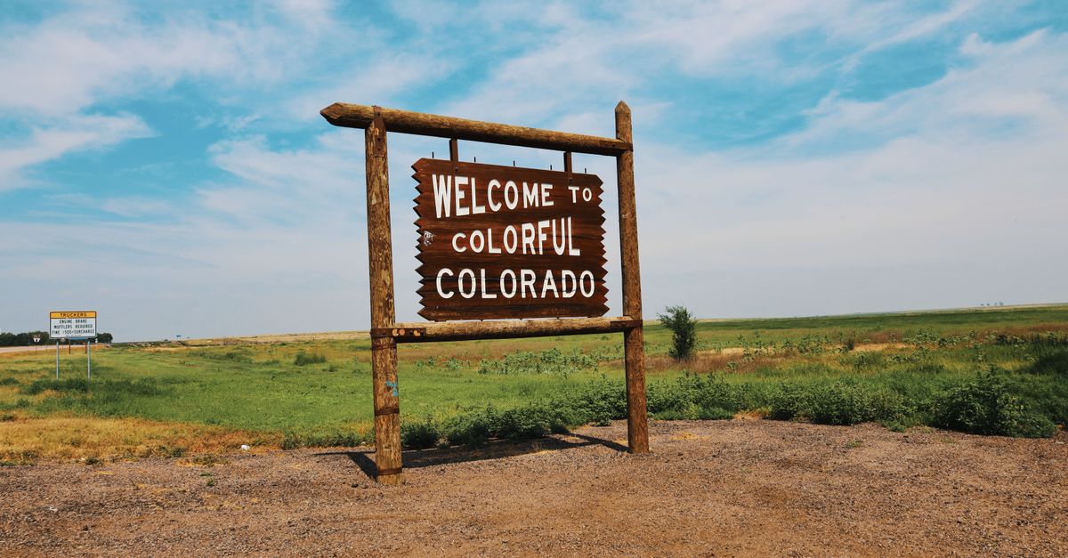Wooden welcome sign in a Colorado field under a bright, clear sky.